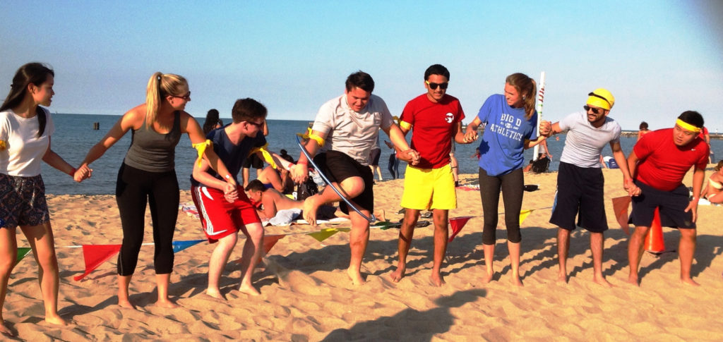 Group of people on a bunch on a sunny day in beach attire playing a hula-hoop game for a team-building event